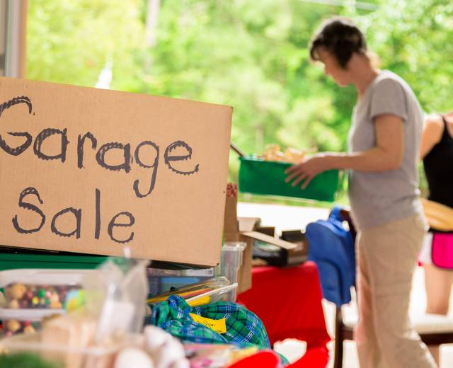 Two women look at items at a garage sale, including a cardboard box